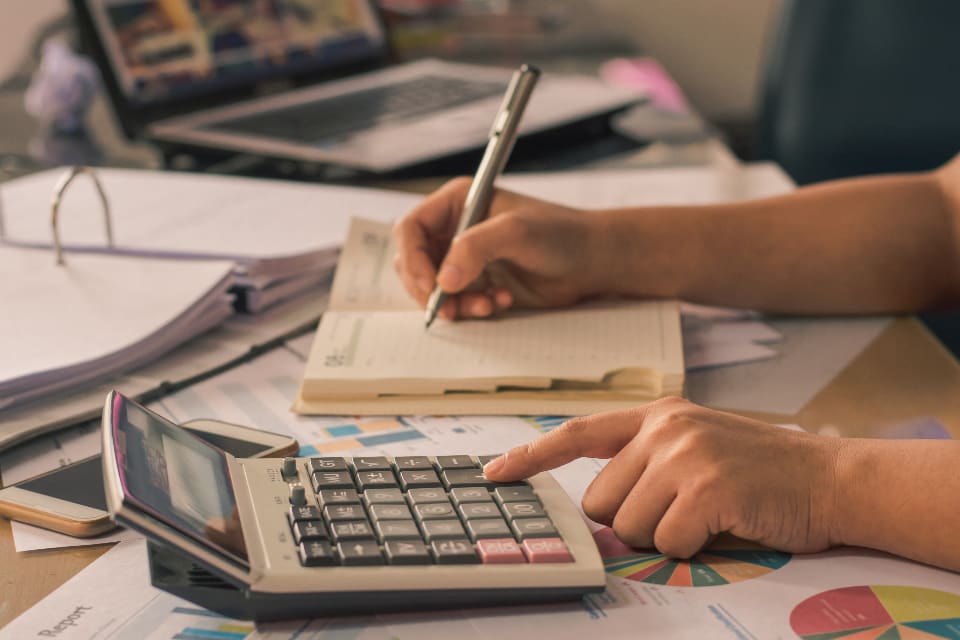 Hand on a calculator beside an open ledger